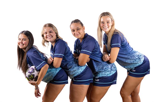 Four players in blue kit leaning in together and laughing