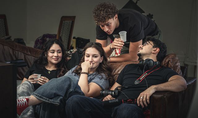 Actors relaxing on a sofa between takes while a crew member leans over them