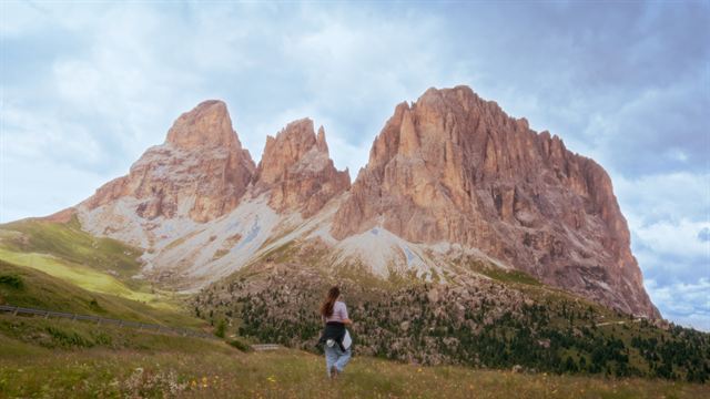 A person walking across a meadow towards a huge rocky peak