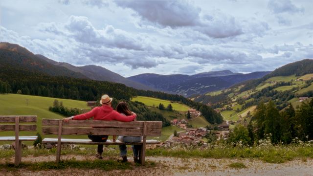 Two people on a bench looking out over a green valley
