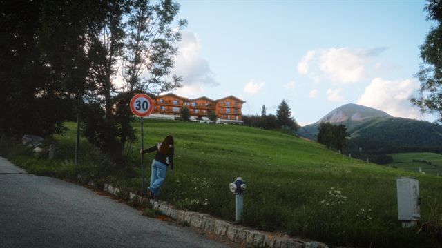 A hotel and a winding road at the foot of a green mountain